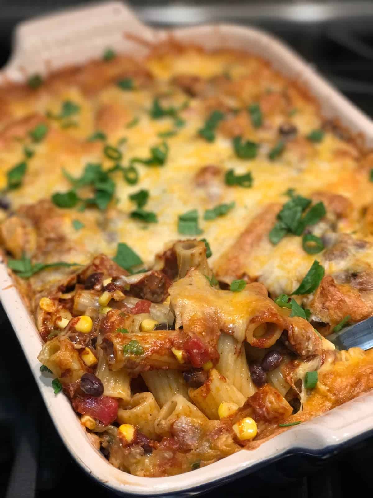 Enchilada Pasta one pot dinner in a baking pan with a spoon pulling out a cheesy spoonful. recipe by foodology geek.