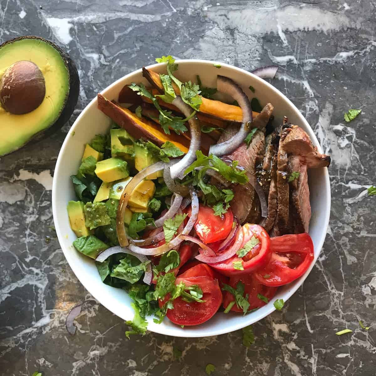 Grilled steak salad bowl with fresh tomatoes, avocados, and sweet potato fries. by foodology geek