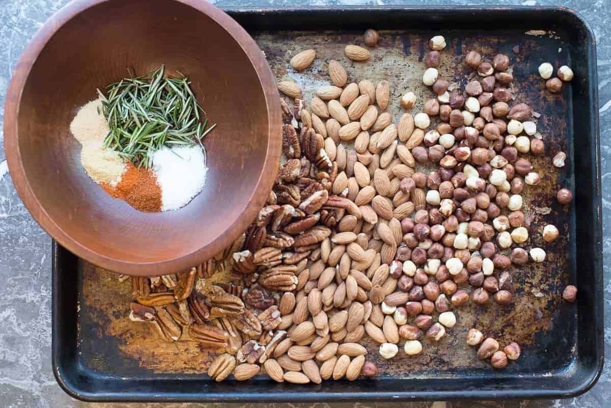 Spiced nuts recipe. Pecans, almonds and hazelnut on a baking sheet with mixed spices and fresh rosemary. by foodology geek
