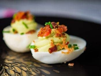 Avocado deviled eggs with crispy bacon, fresh tomatoes and chives.