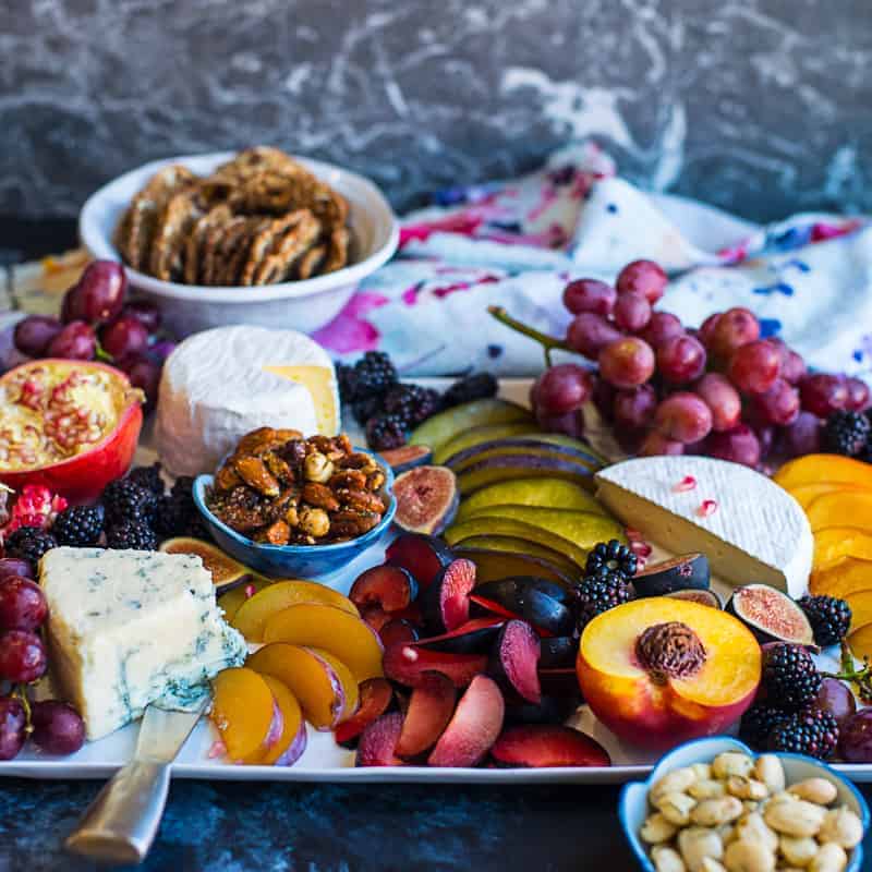 gourmet cheese board with stone fruit, pomegranate, roasted nuts, blue cheese, brie, and dried fruits.