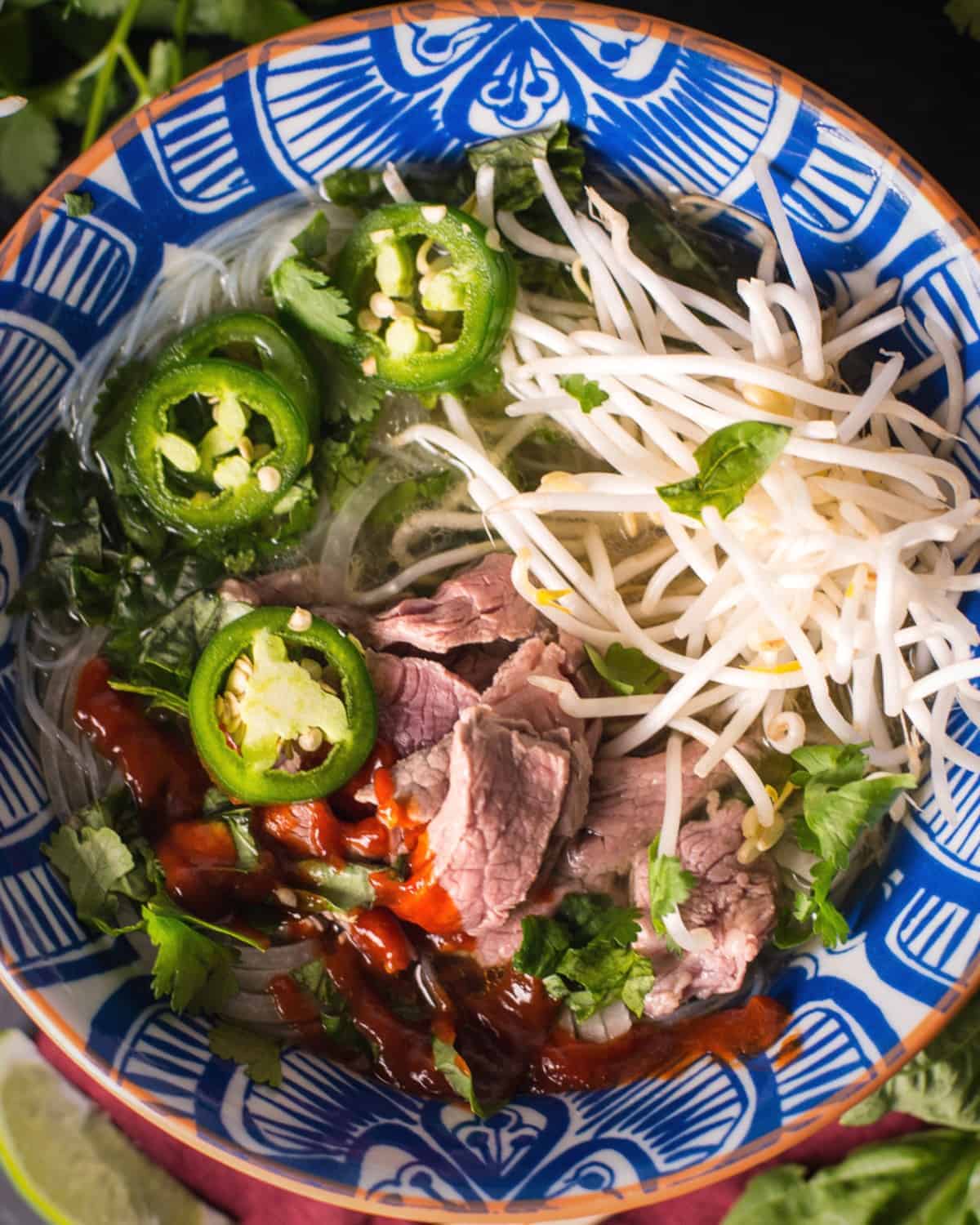 pho tai served in a large bowl with bean sprouts, jalapenos, and plenty of sriracha