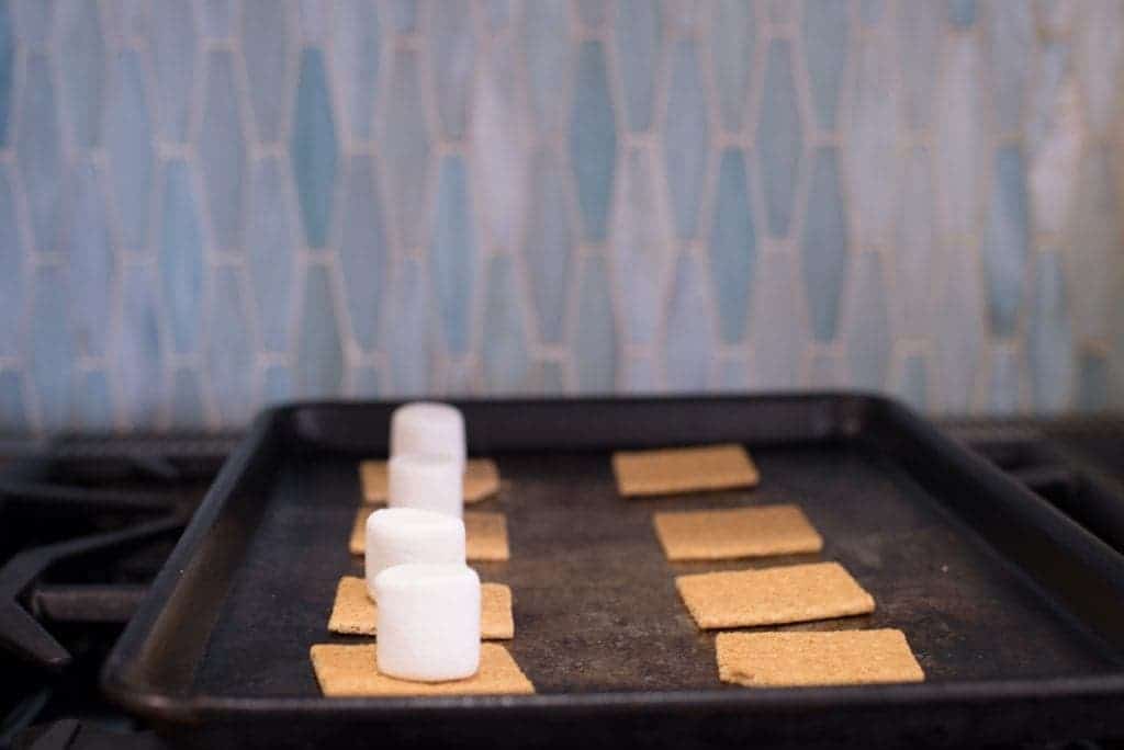 How to make s'mores in the oven: baking sheet with graham crackers and marshmallows.