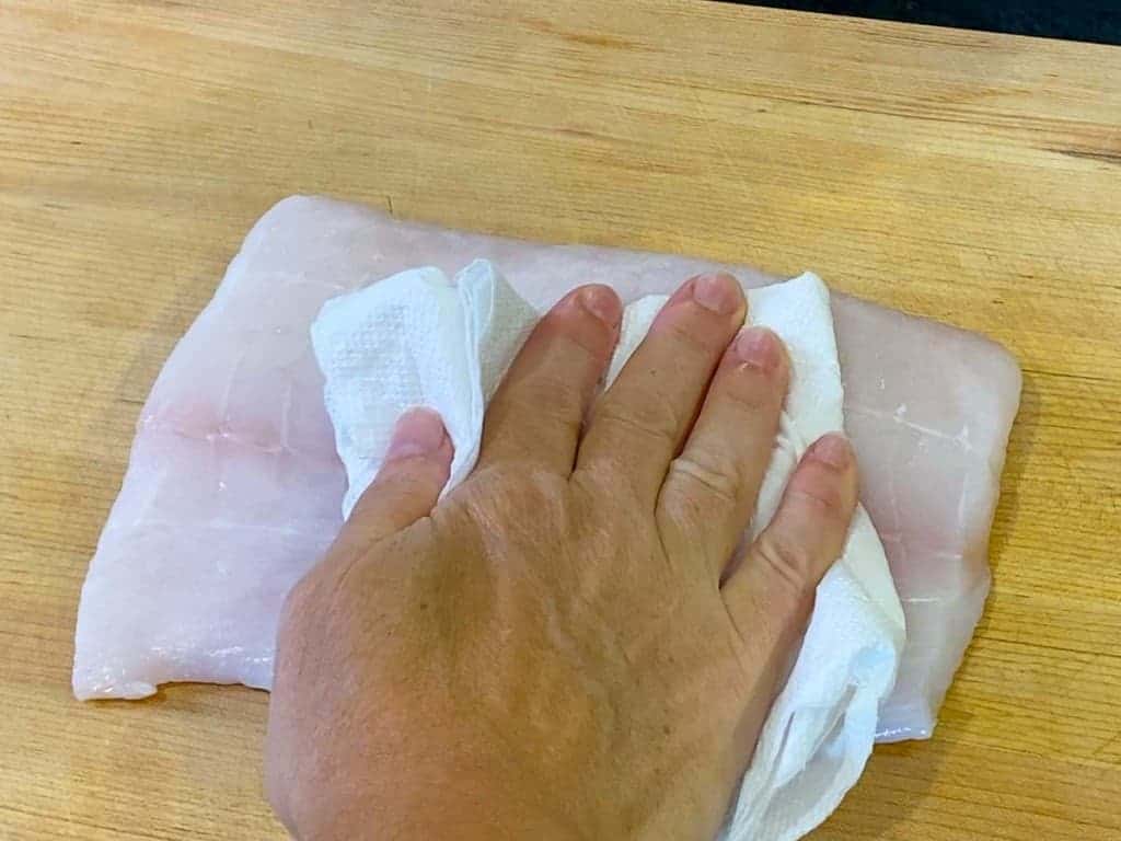 A halibut filet being patted dry with a paper towel.