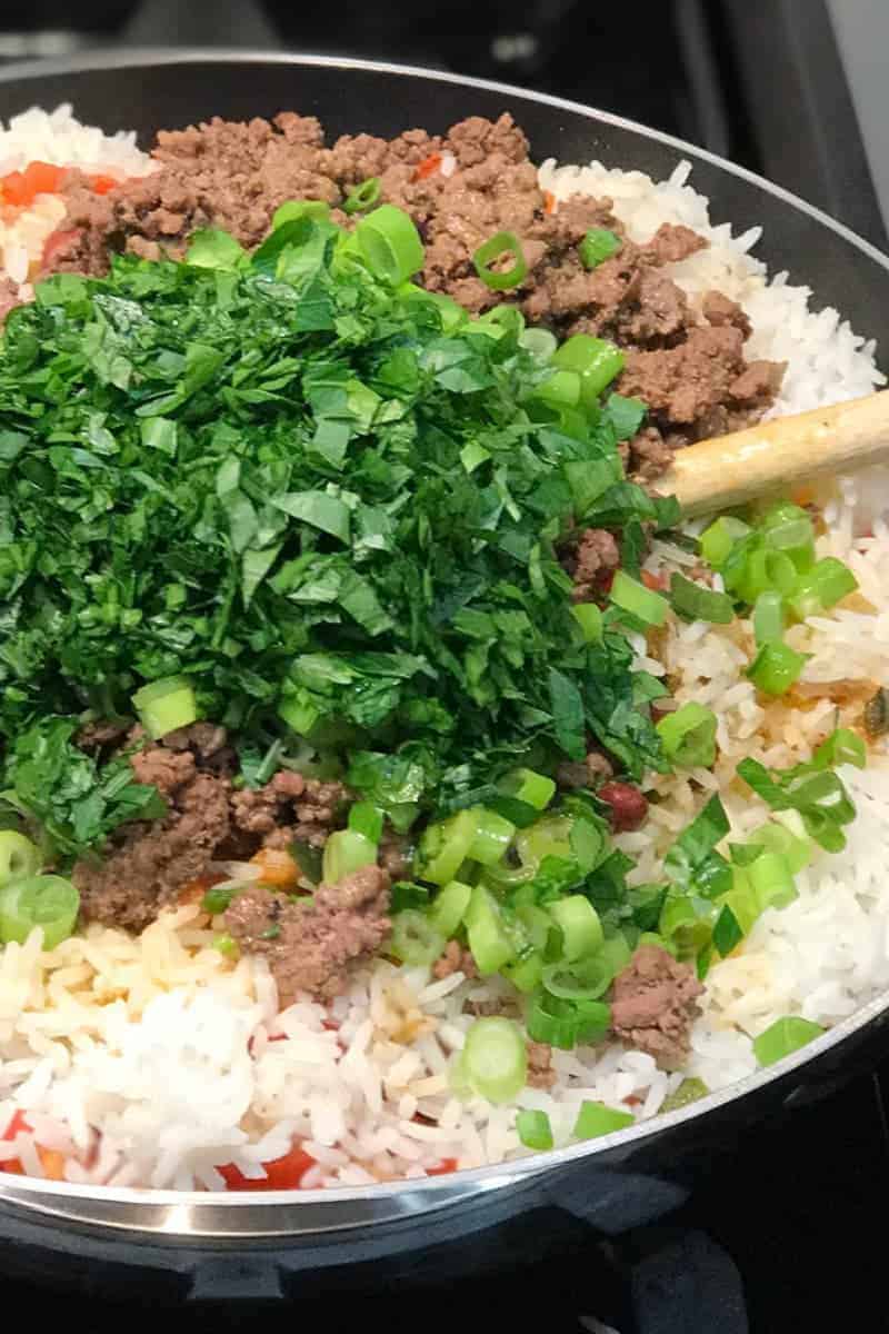 Making Puerto Rican Dirty Rice - add ground beef and fresh veggies, then toss well until combined.