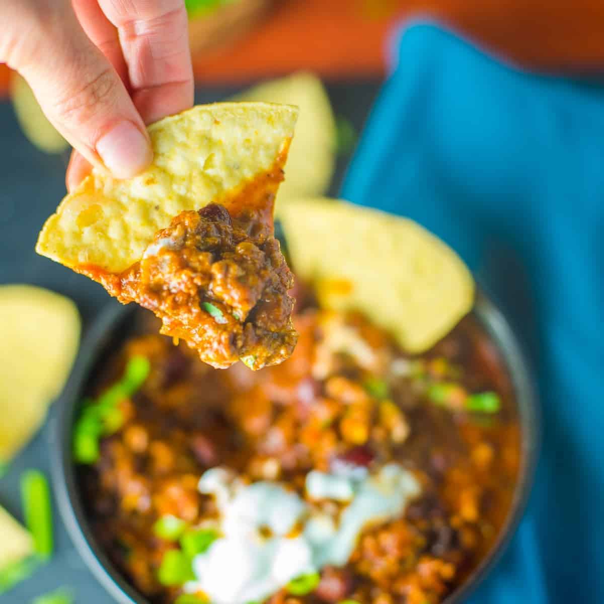 a bowl of chili con carne with tortilla chips, sour cream and green onions.