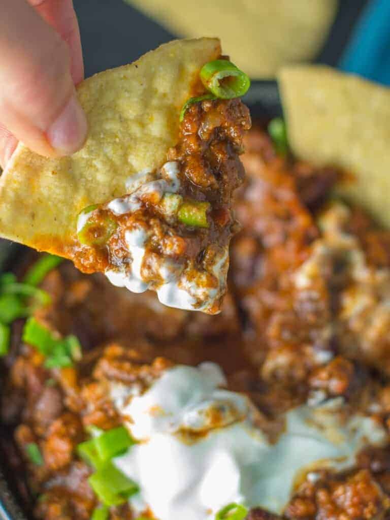 a tortilla chip with chili and sour cream on it.