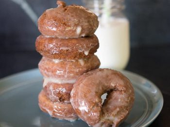 Stack of glazed pumpkin donuts with a tall cold glass of milk.