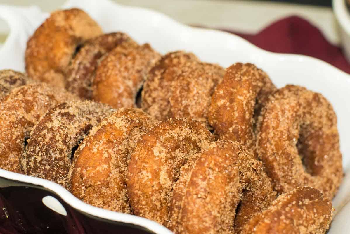 A dozen apple cider donuts covered in cinnamon sugar, in a black and white dish.