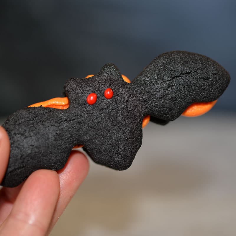 Bat shaped cookie with red royal icing eyes, filled with orange butter cream. These are gourmet oreo cookies that are shaped like bats.