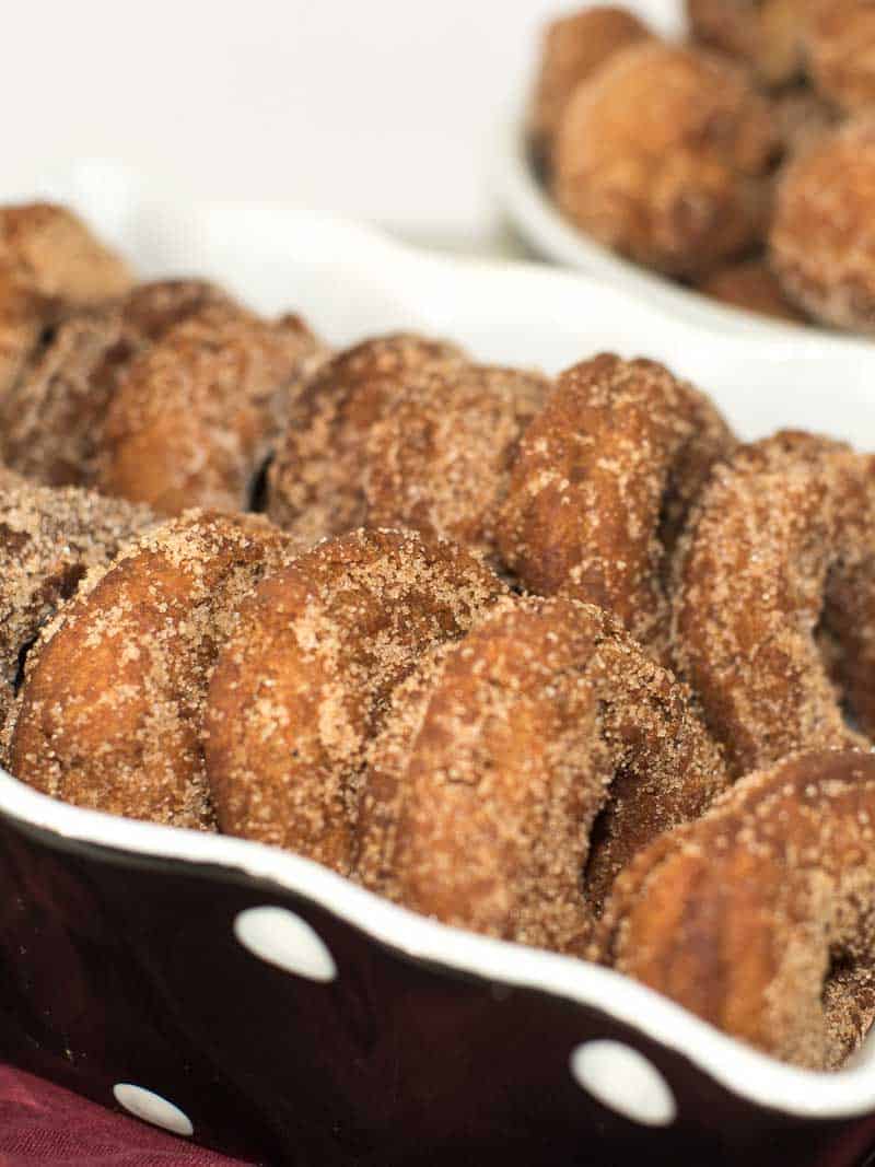 Homemade apple cider donuts dusted with cinnamon and sugar in a black and white polka dot dish.