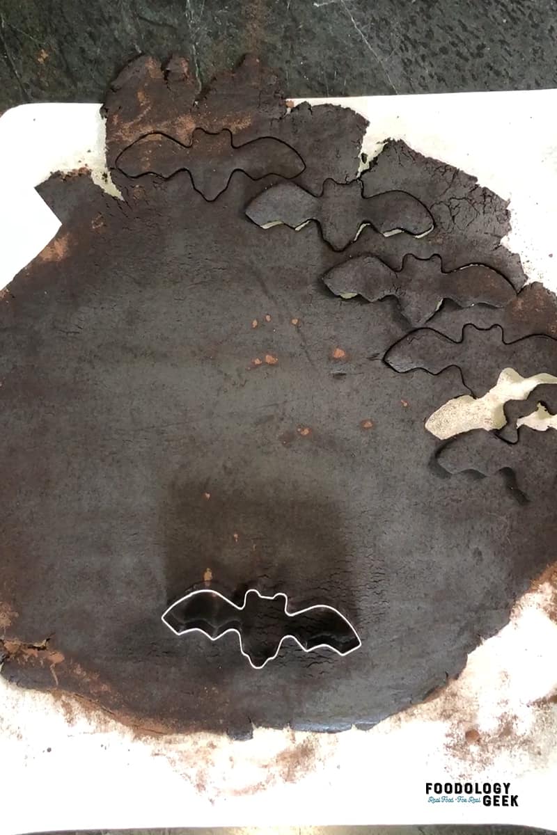 Bat cut out cookies being cut out of chocolate sugar cookie dough. 