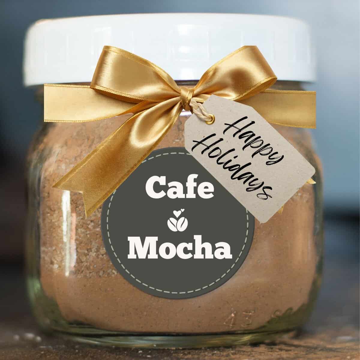 Jar of homemade Café Mocha Hot Chocolate Mix decorated with a gold ribbon and a “Happy Holidays” gift tag.