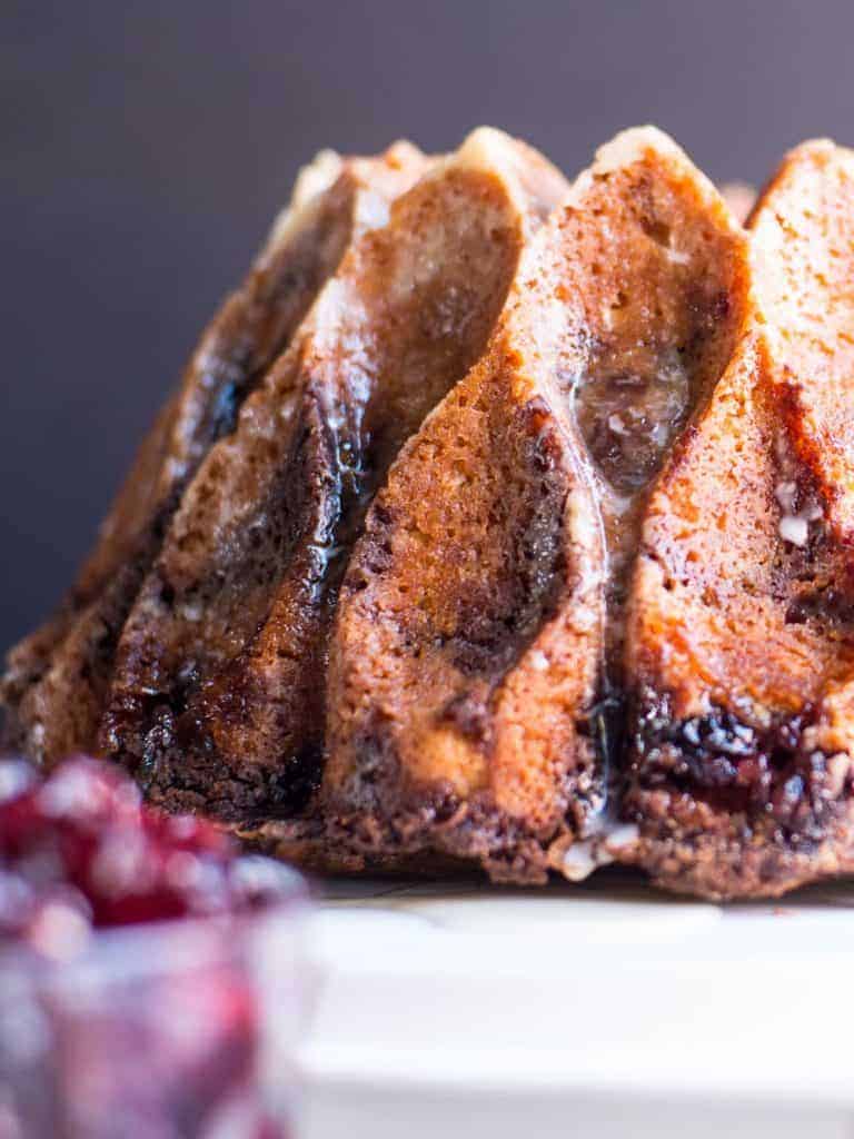 Cranberry and Cinnamon Sour Cream Coffee Cake with a Grand Marnier Glaze. Made in a bundt pan and set on a white cake pan.