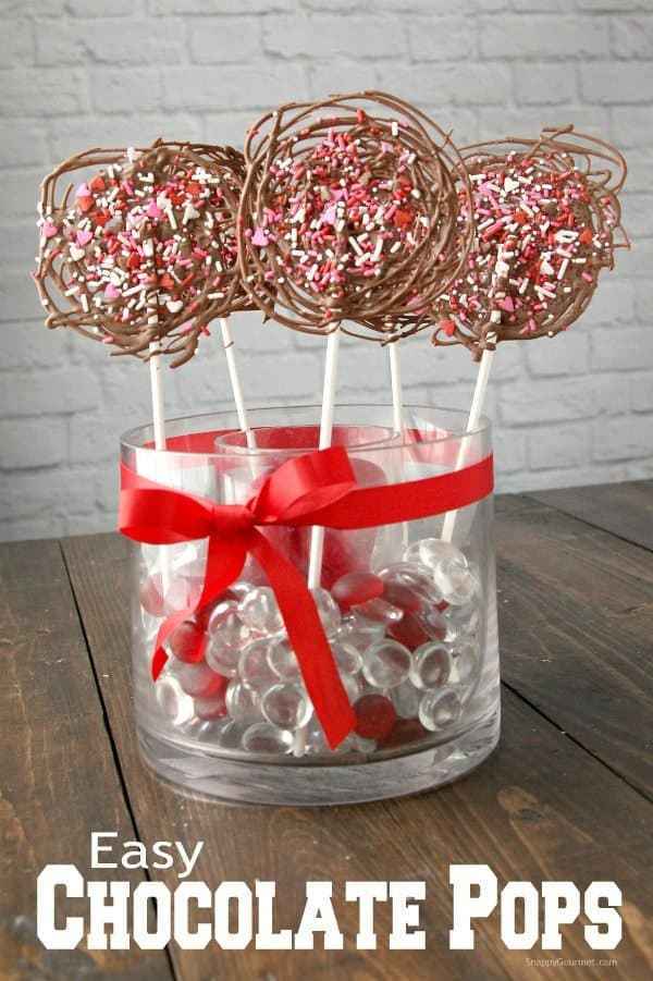 Homemade chocolate lollipops made by drizzling melted chocolate in a circular pattern and then topping with valentines day sprinkles.