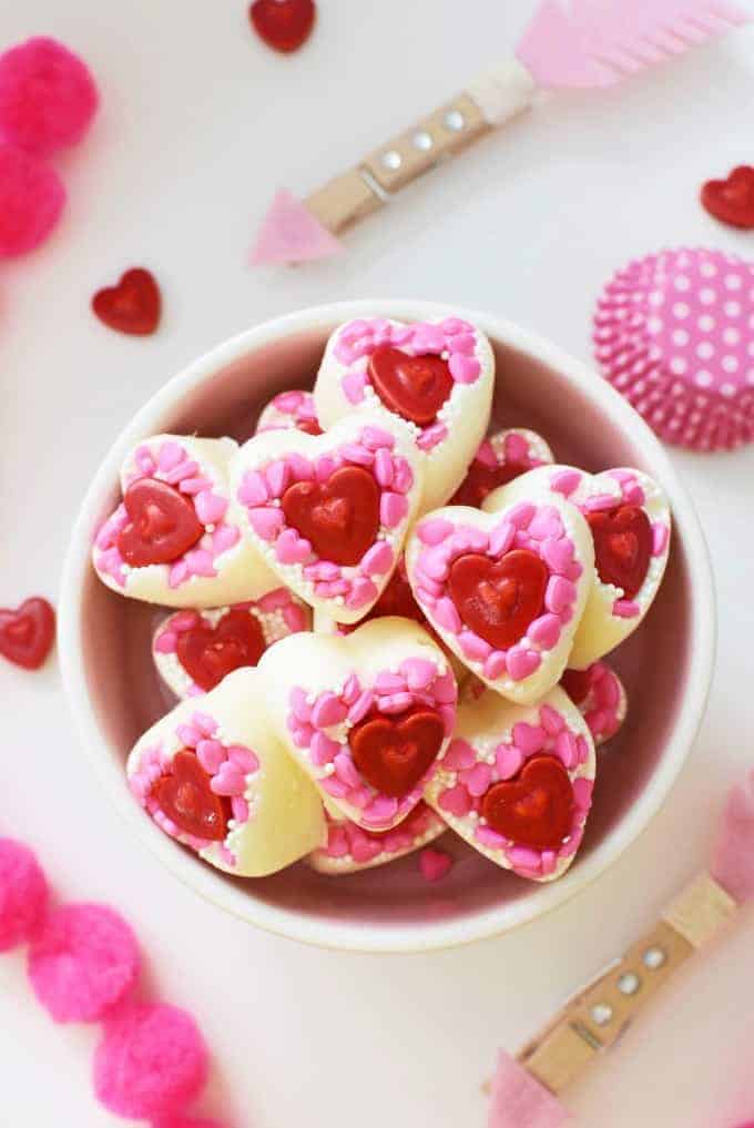 Homemade white chocolate Valentine's Day candies. Made from melted candy and sprinkled. #valentinesdaycandy #homemade #whitechocolate A bowl of homemade white chocolate heart candies topped with pink and red heart-shaped sprinkles.