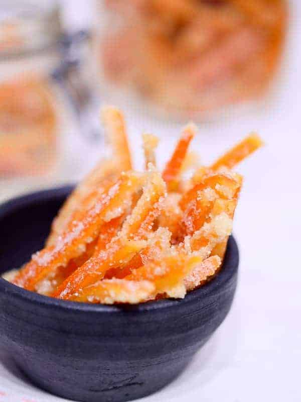 Candied orange peel in a bowl with jars of candied orange peel behind