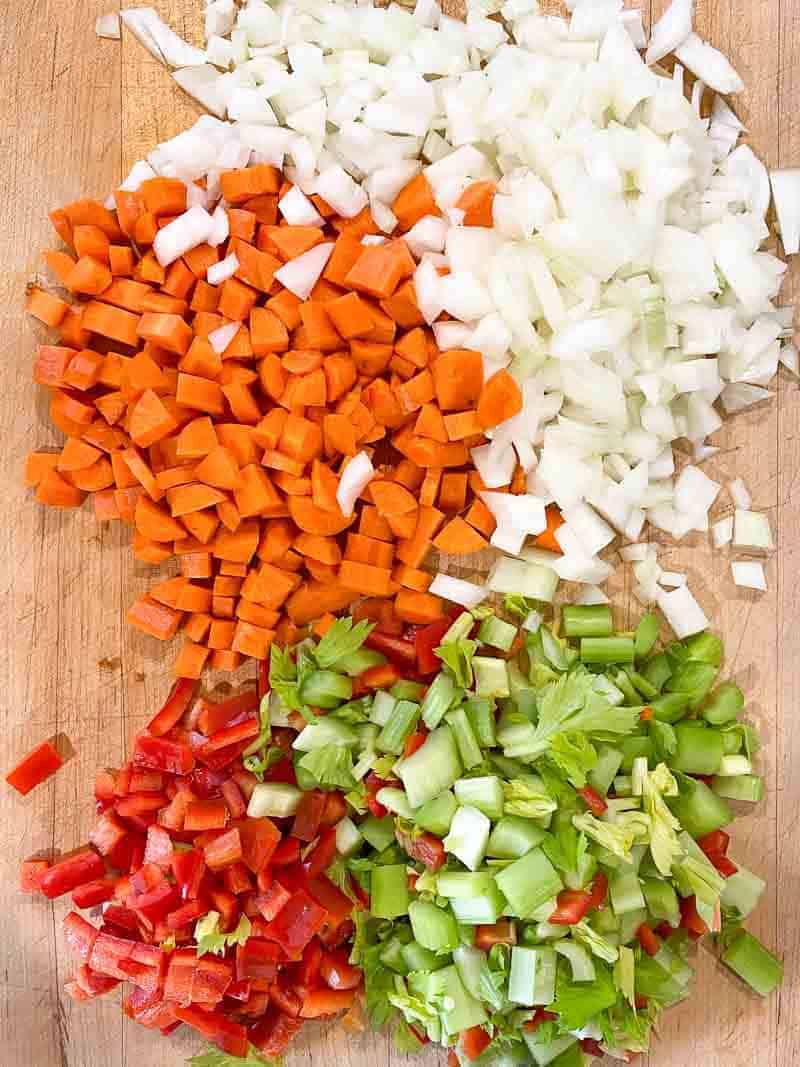 Mirepoix on a cutting board. carrots, onions, celery, and red peppers.