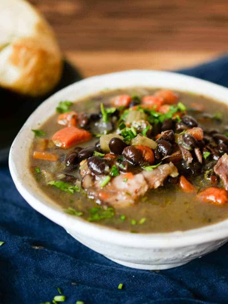 Black bean and ham soup in a white bowl served with crusty french bread.