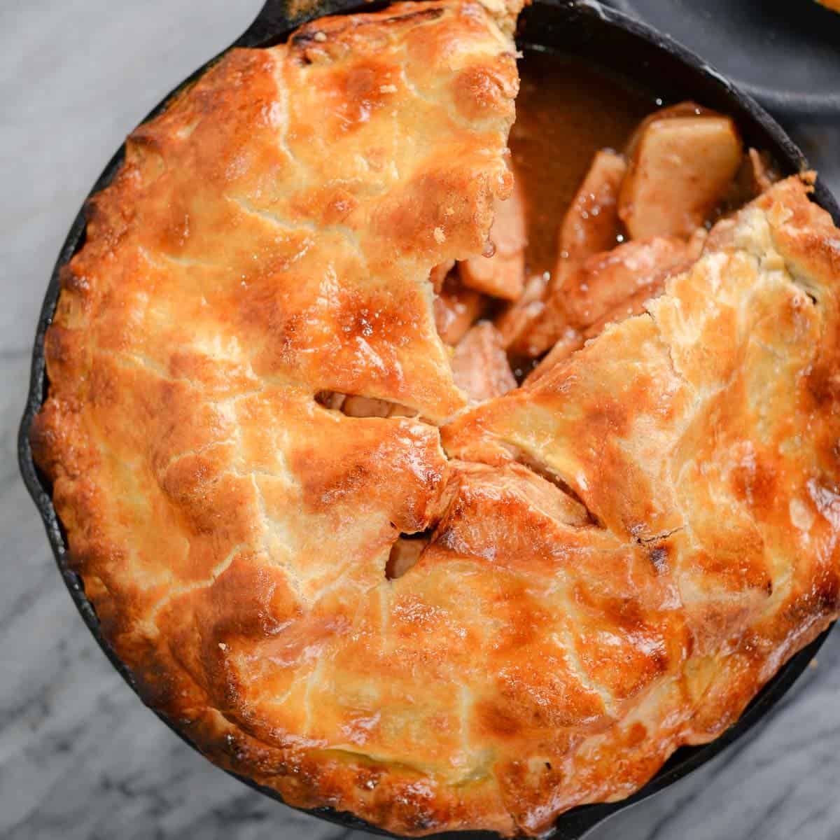 apple pie baked in a cast iron pan with a slice cut out
