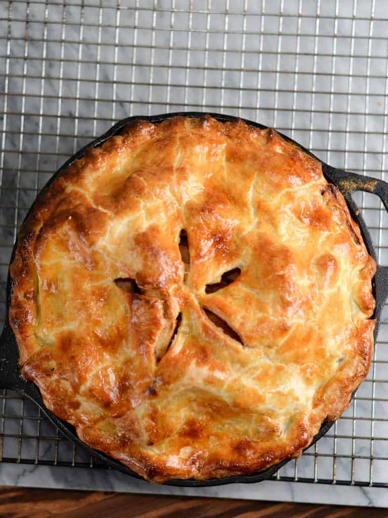 apple pie baked in a cast iron skillet cooling on a wire baking rack.