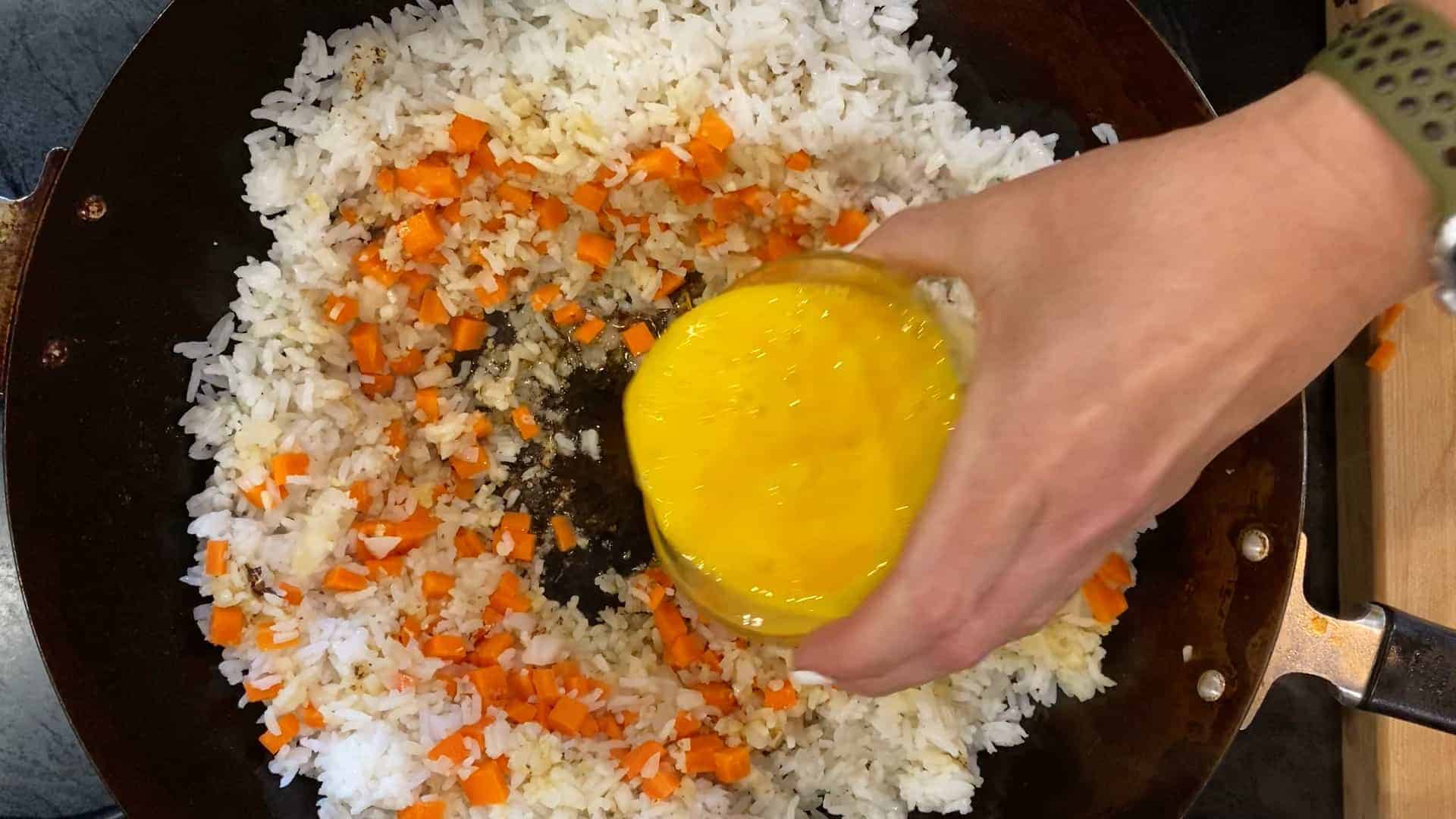 fried rice with egg in a wok. Egg being poured into the wok before scrambling.