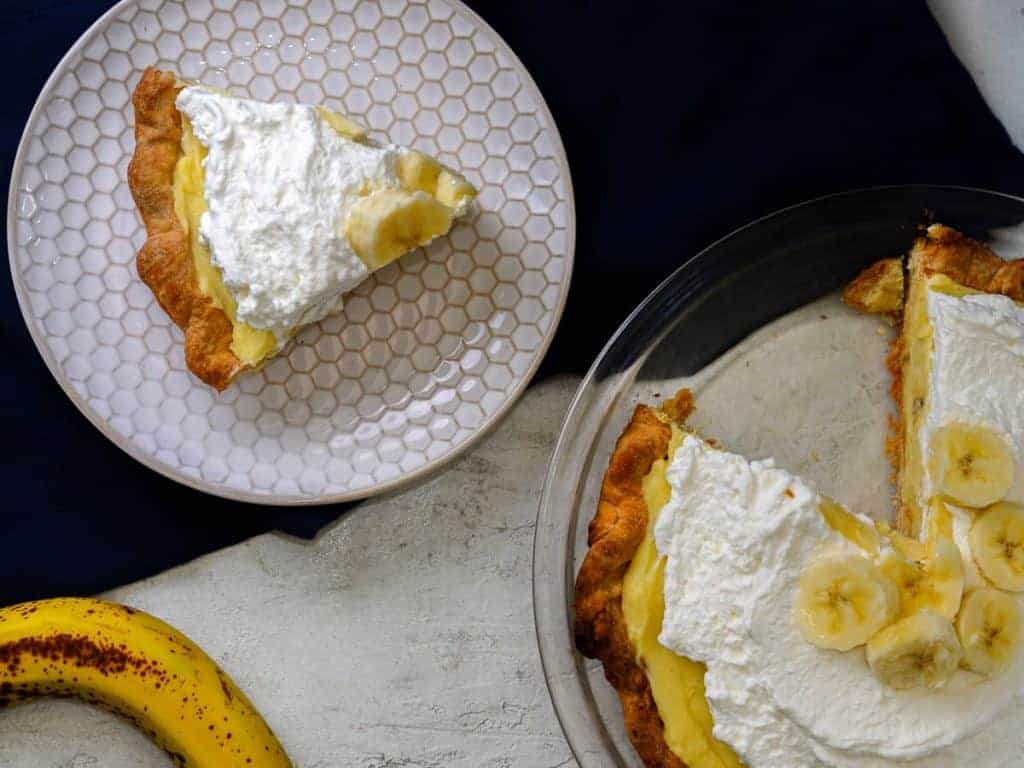 Slice of banana cream pie next to the full banana cream pie.