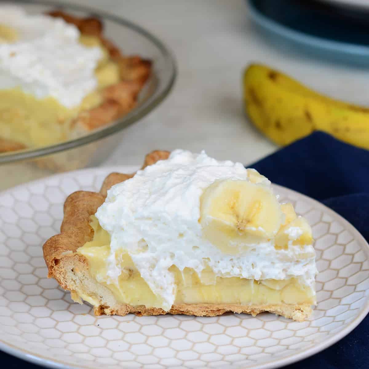 slice of fresh banana cream pie. topped with whipped cream and more fresh bananas.