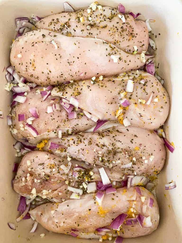 chicken breasts with lemon, oregano, and garlic marinade in a dish