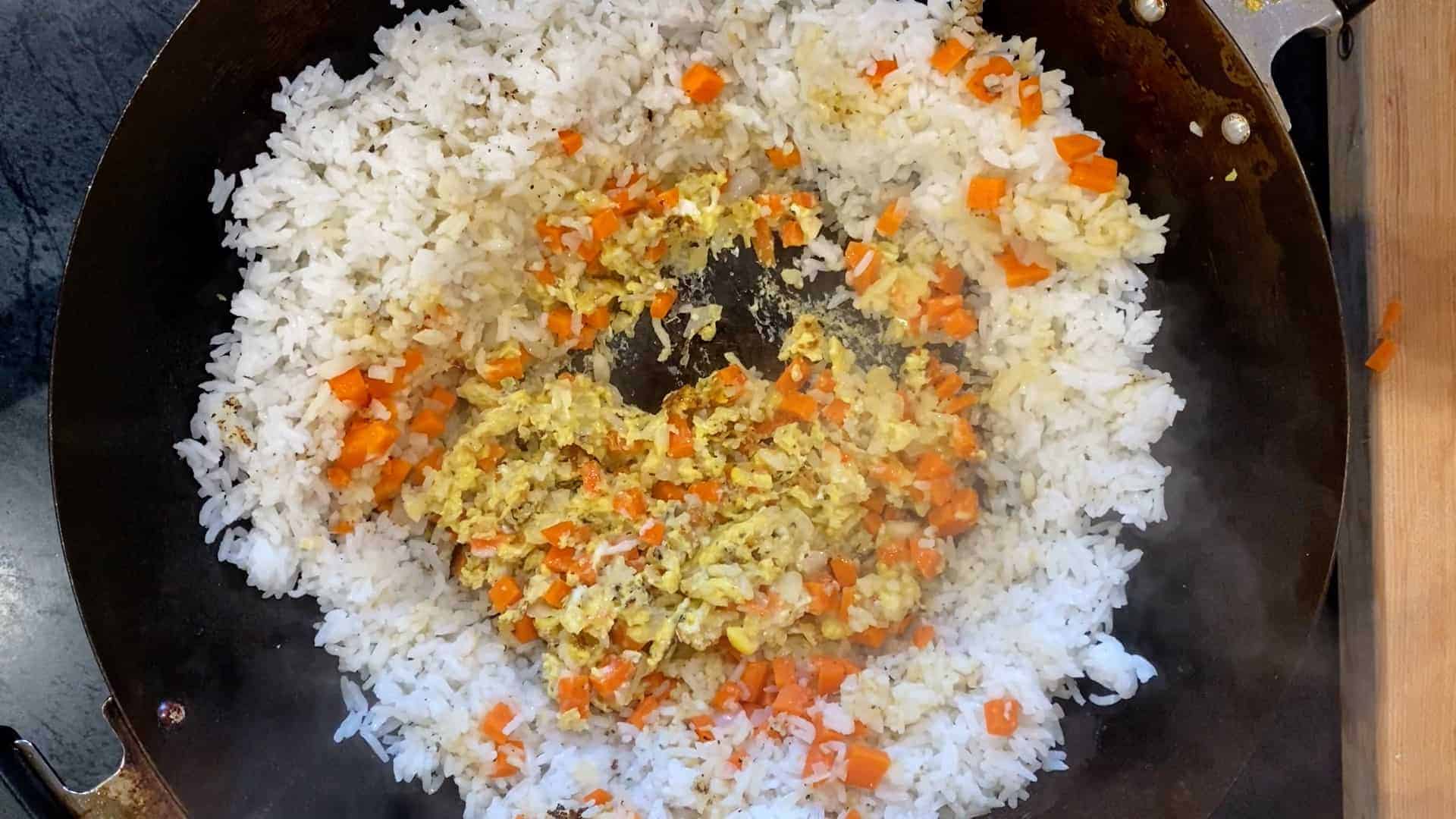 how to make plain fried rice. rice in a wok with carrots, onions, garlic, and eggs