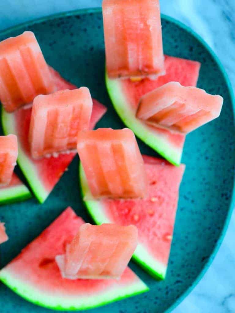 frozen watermelon ice pops on a platter with fresh watermelon slices.