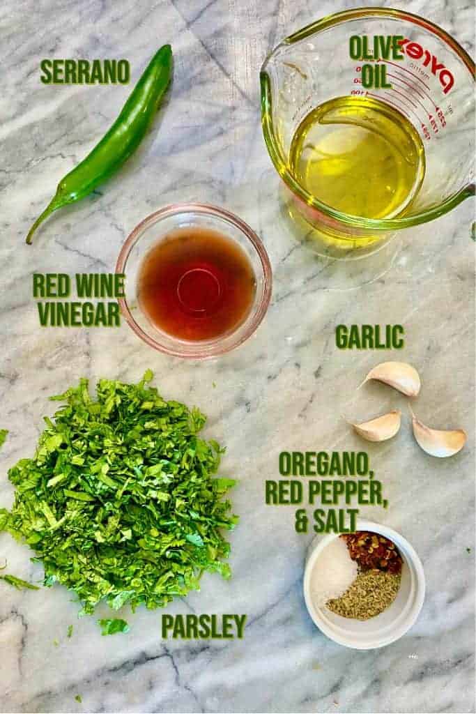 Ingredient for chimichurri sauce layed out on a marble counter top. 