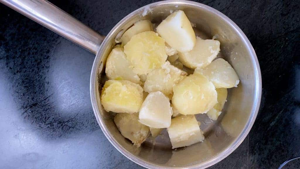 Quarter the potatoes and place them in the water. Bring to a boil and then reduce the heat slightly. Boil until they are soft about 15 minutes. Drain. Peel the skins off and return them back to the pot. 