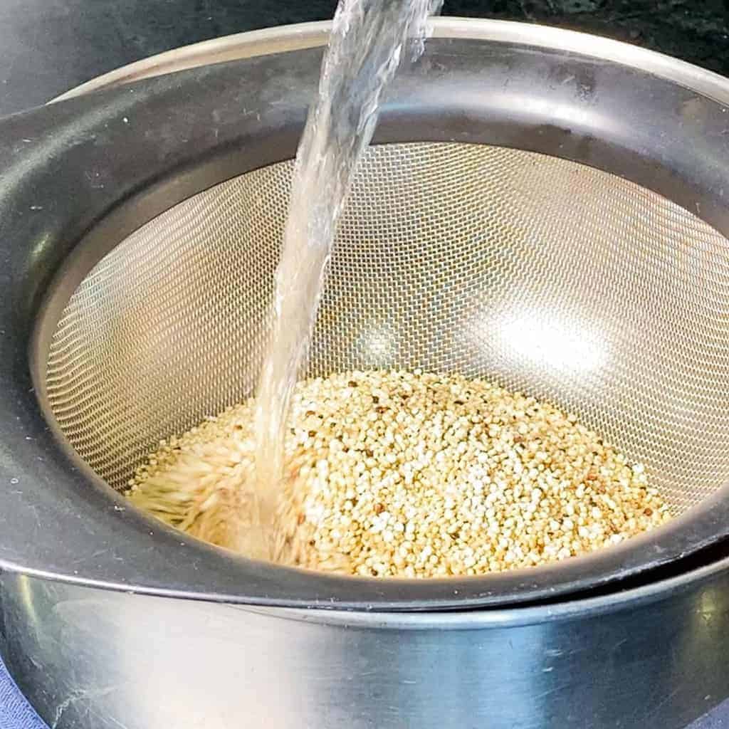 quinoa in a fine mesh strainer being rinsed with water. 