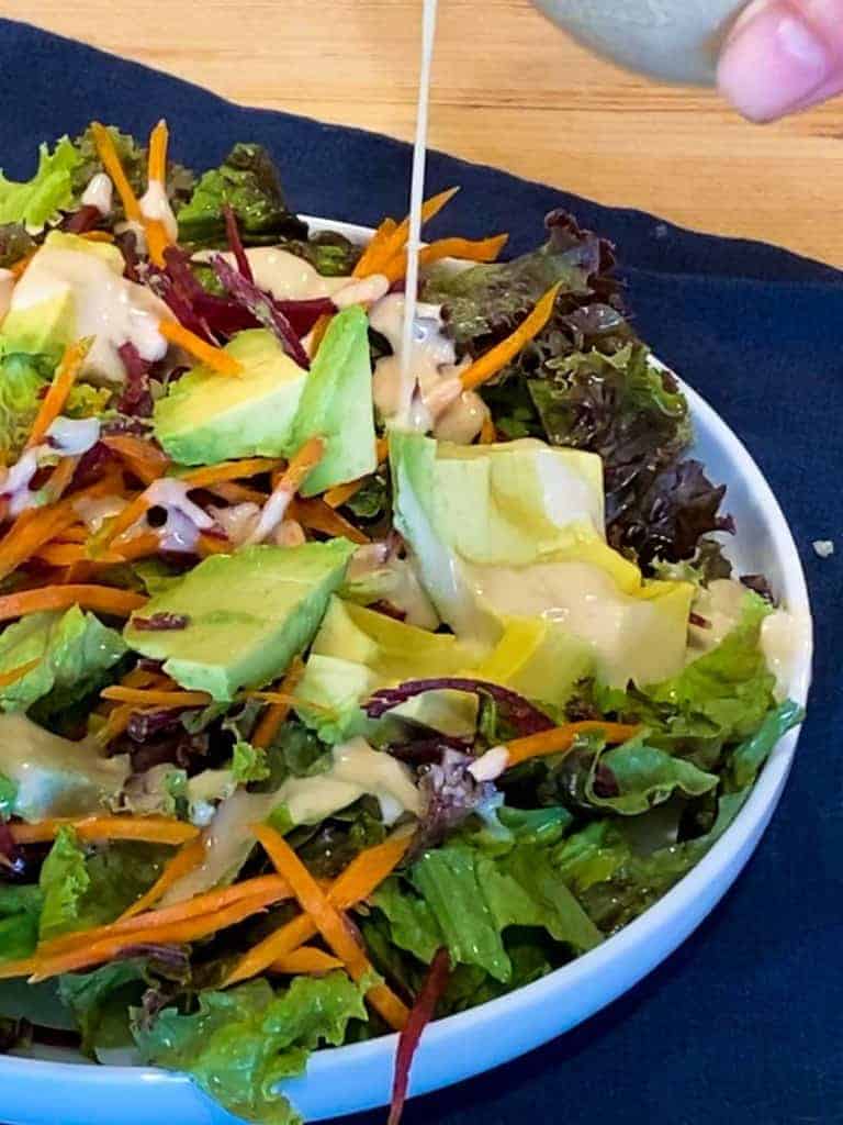 pouring tahini dressing on a salad