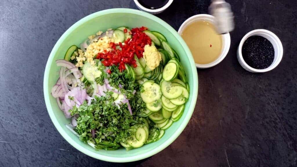 All of the ingredients for making Spicy Asian Cucumber Salad in a green bowl. 