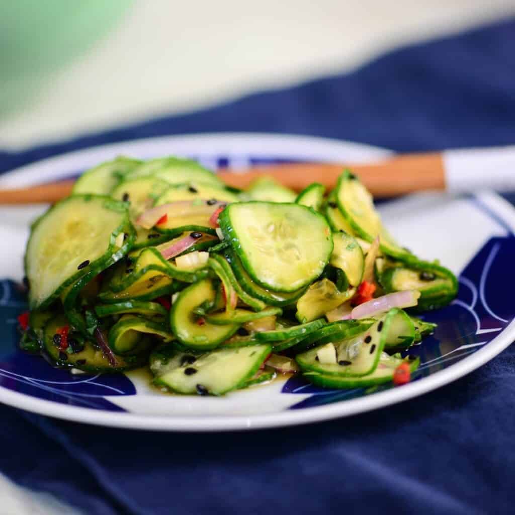 asian cucumber salad recipe in a blue and white bowl with chopsticks