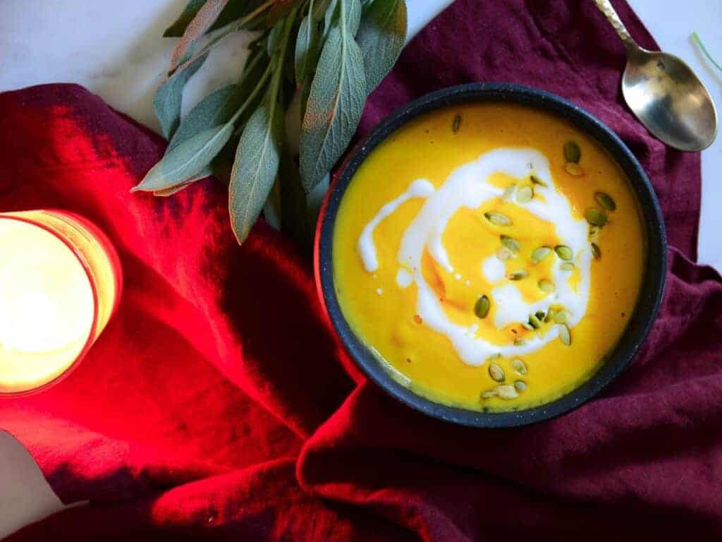 butternut squash soup with sage on a table with a red napkin and candles