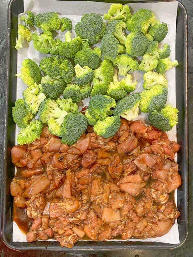 broccoli and marinated chicken on a prchment lined baking sheet