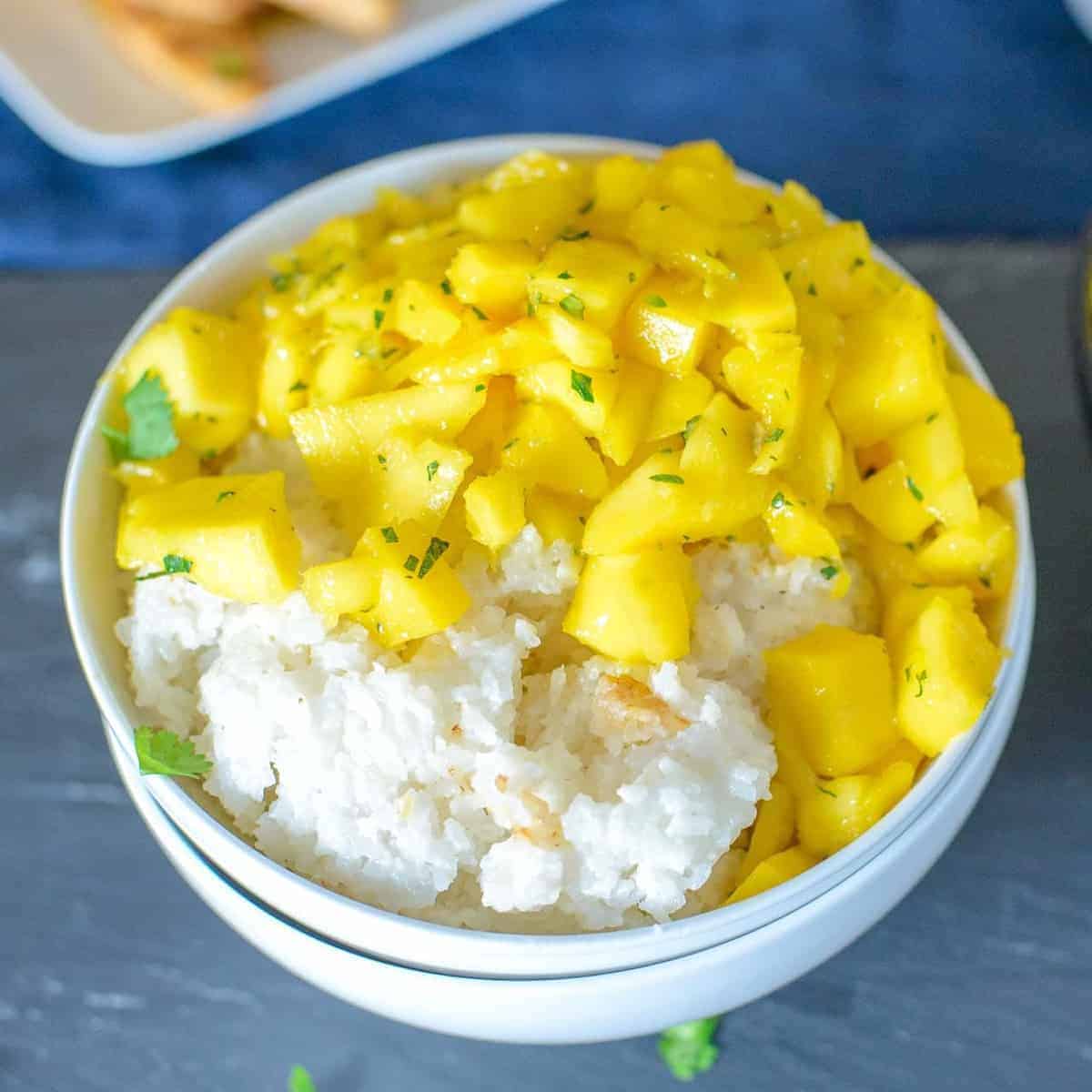 coconut sticky rice topped with fresh mangoes and chopped mint in a white bowl