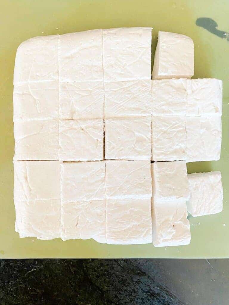 Fresh homemade keto marshmallows being sliced on a cutting mat. 