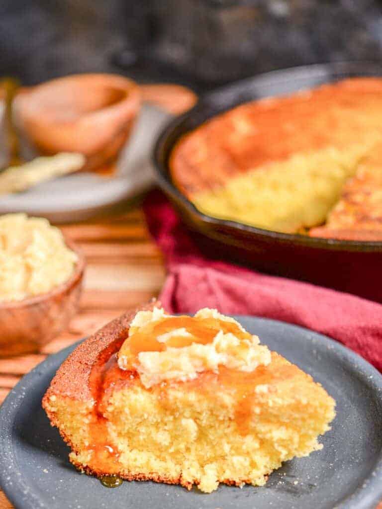 Fluffy homemade buttermilk cornbread recipe. Pictured in a cast iron skillet with a slice cut out and served with fresh wihipped honey butter. 