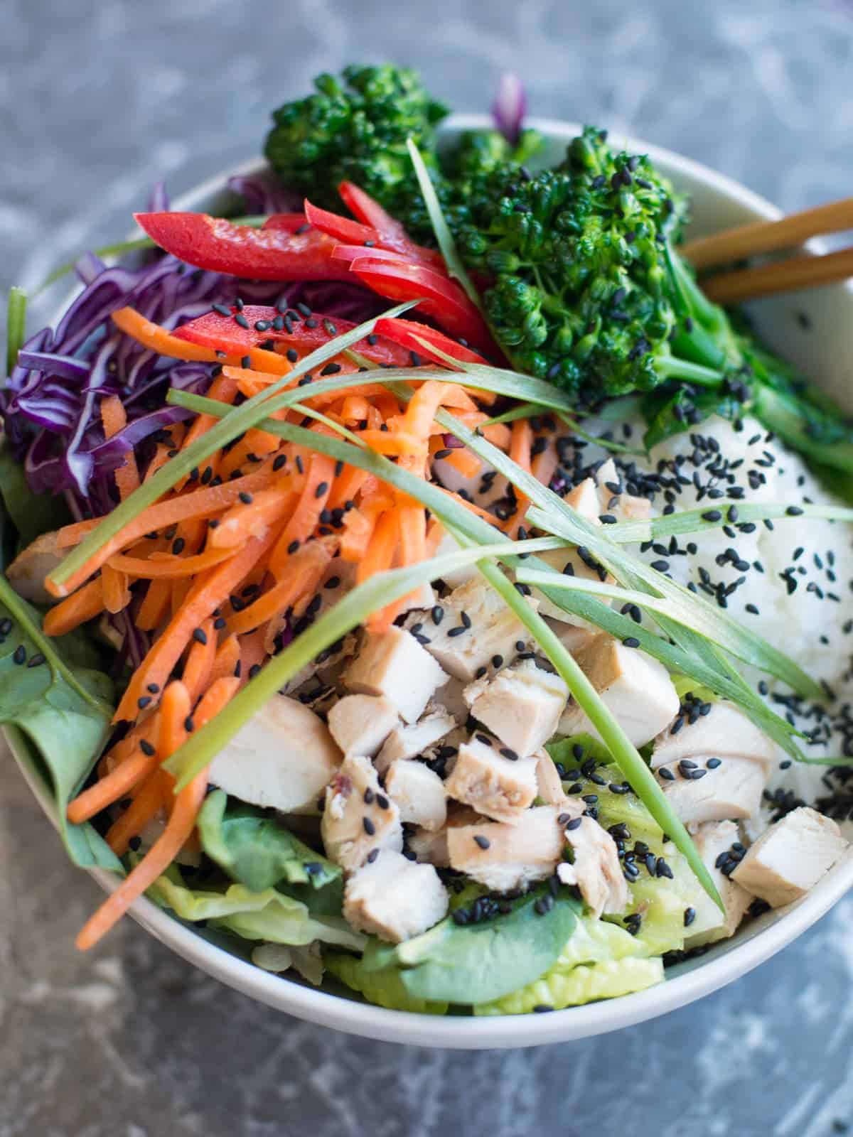 healthy chicken teriyaki meal prep bowl topped with lots of fresh veggies and asian salad dressing