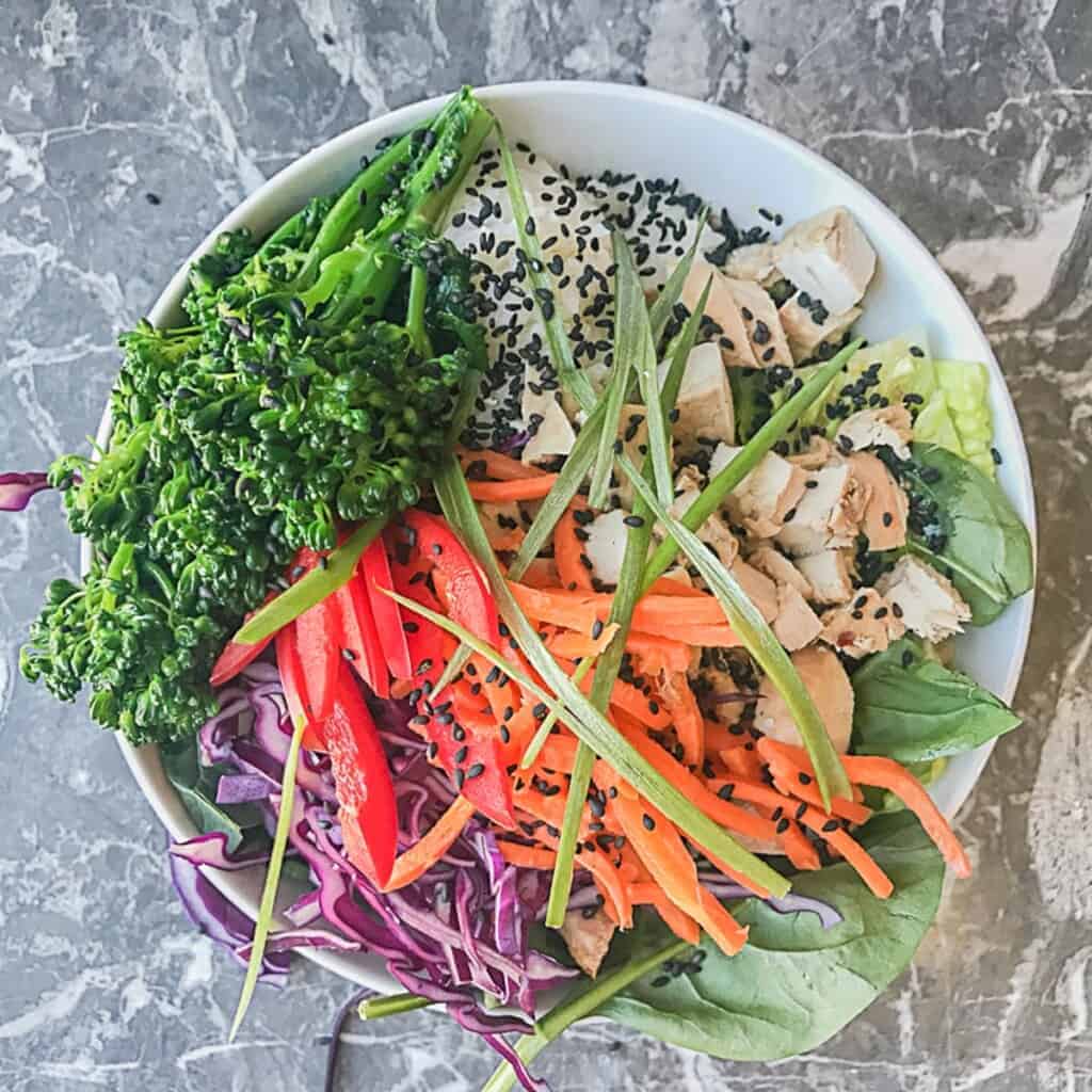 lettuce and spinach with sesame ginger dressing and a scoop of sushi rice and teriyaki chicken, red cabbage, carrots, red peppers, broccoli, green onions, and sesame seeds