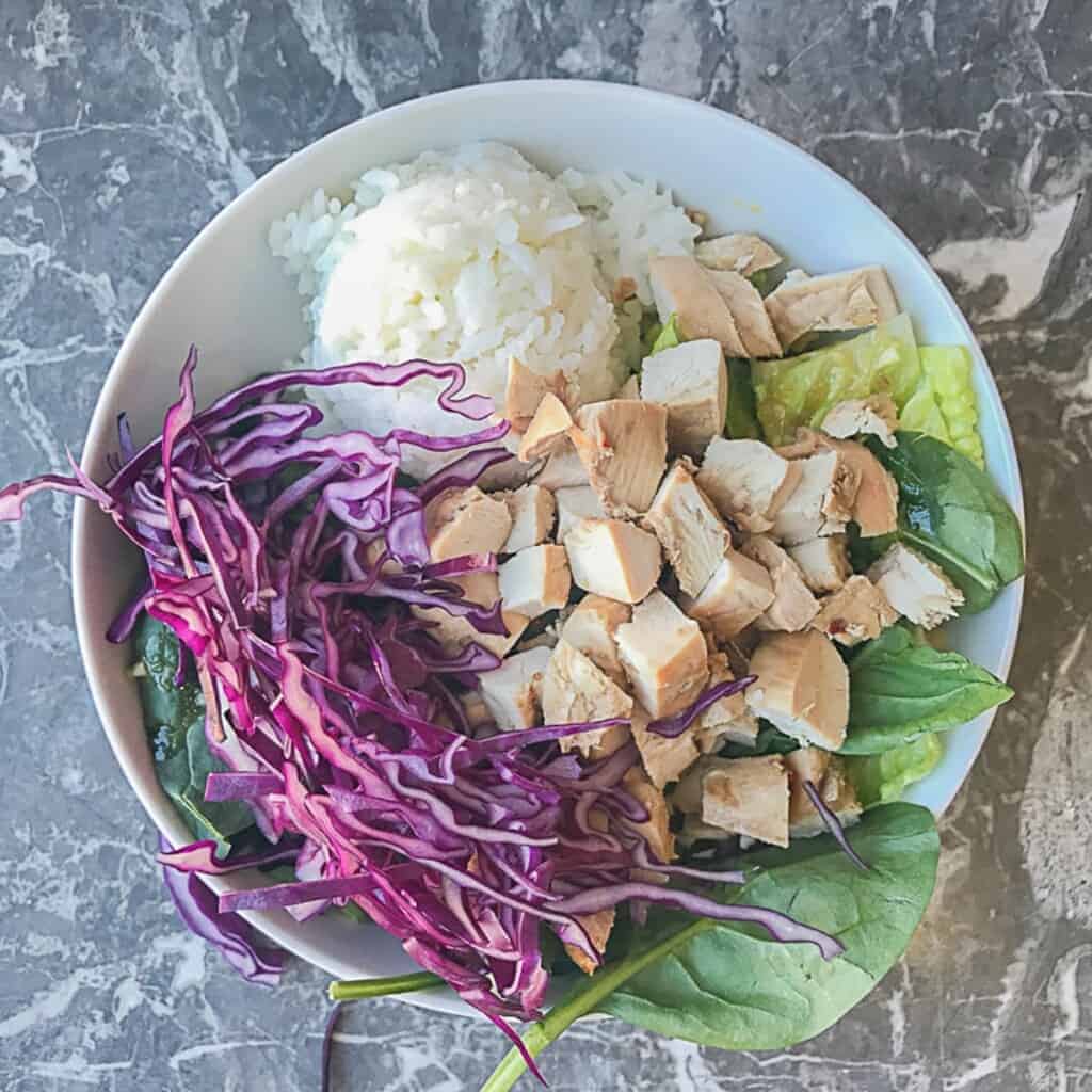 lettuce and spinach with sesame ginger dressing and a scoop of sushi rice and teriyaki chicken and red cabbage