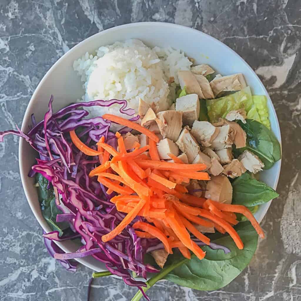 lettuce and spinach with sesame ginger dressing and a scoop of sushi rice and teriyaki chicken, red cabbage, and carrots