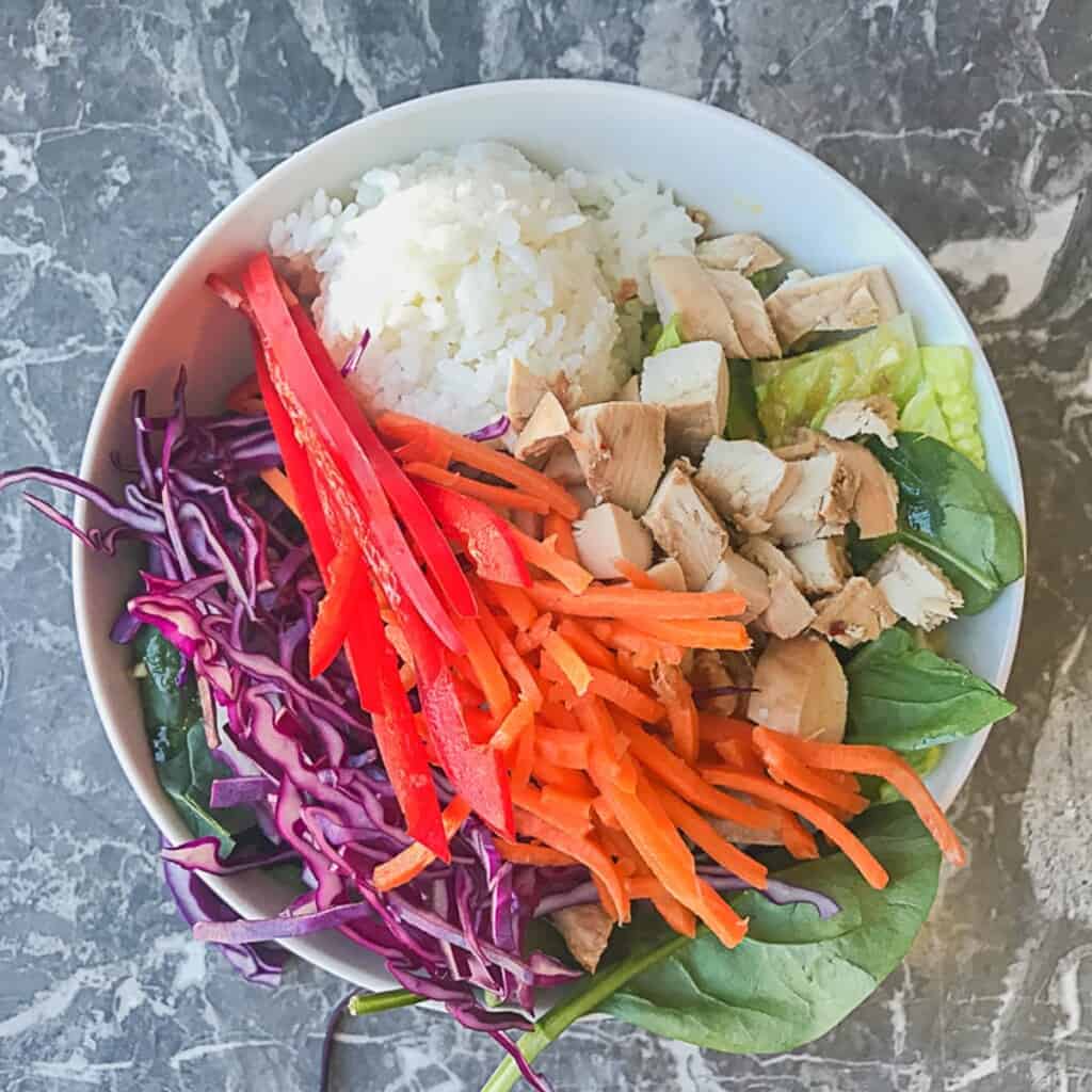 lettuce and spinach with sesame ginger dressing and a scoop of sushi rice and teriyaki chicken, red cabbage, carrots, and red peppers