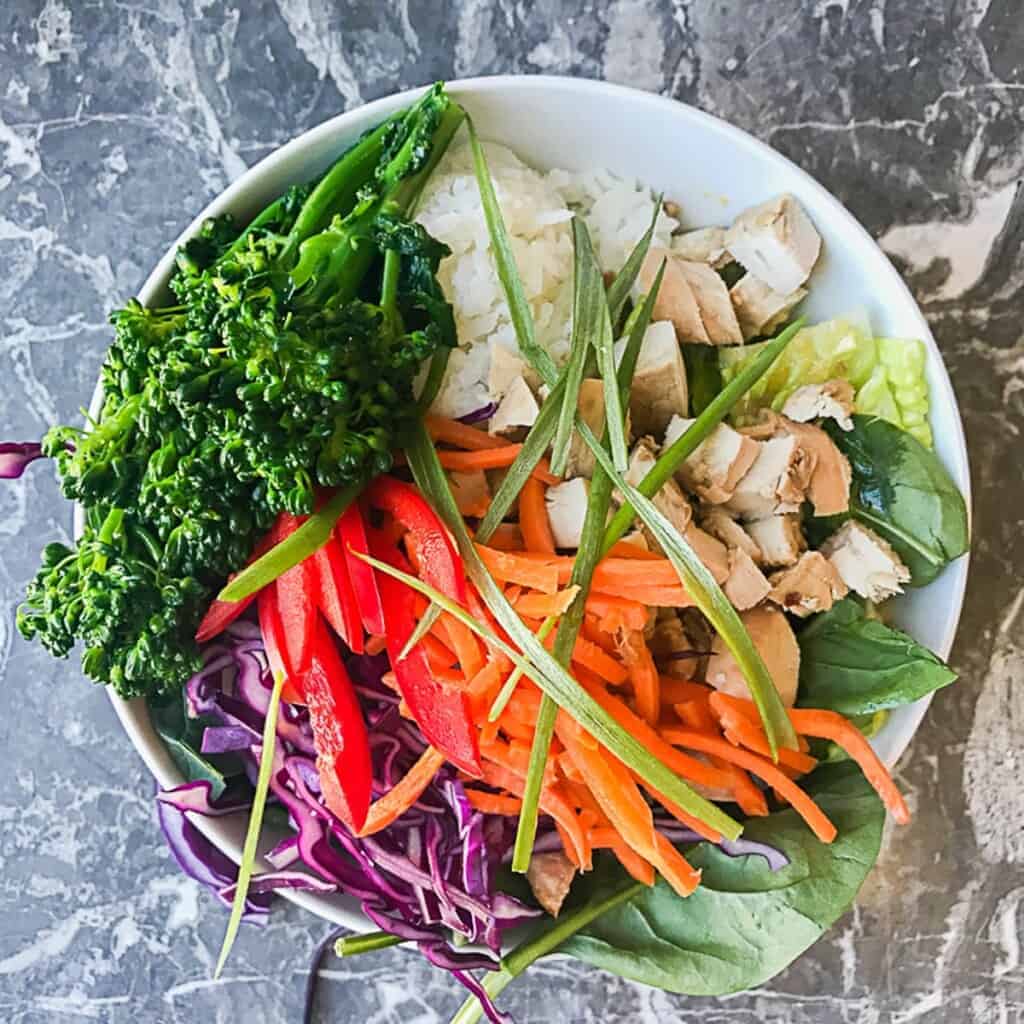lettuce and spinach with sesame ginger dressing and a scoop of sushi rice and teriyaki chicken, red cabbage, carrots, red peppers, broccoli and green onions