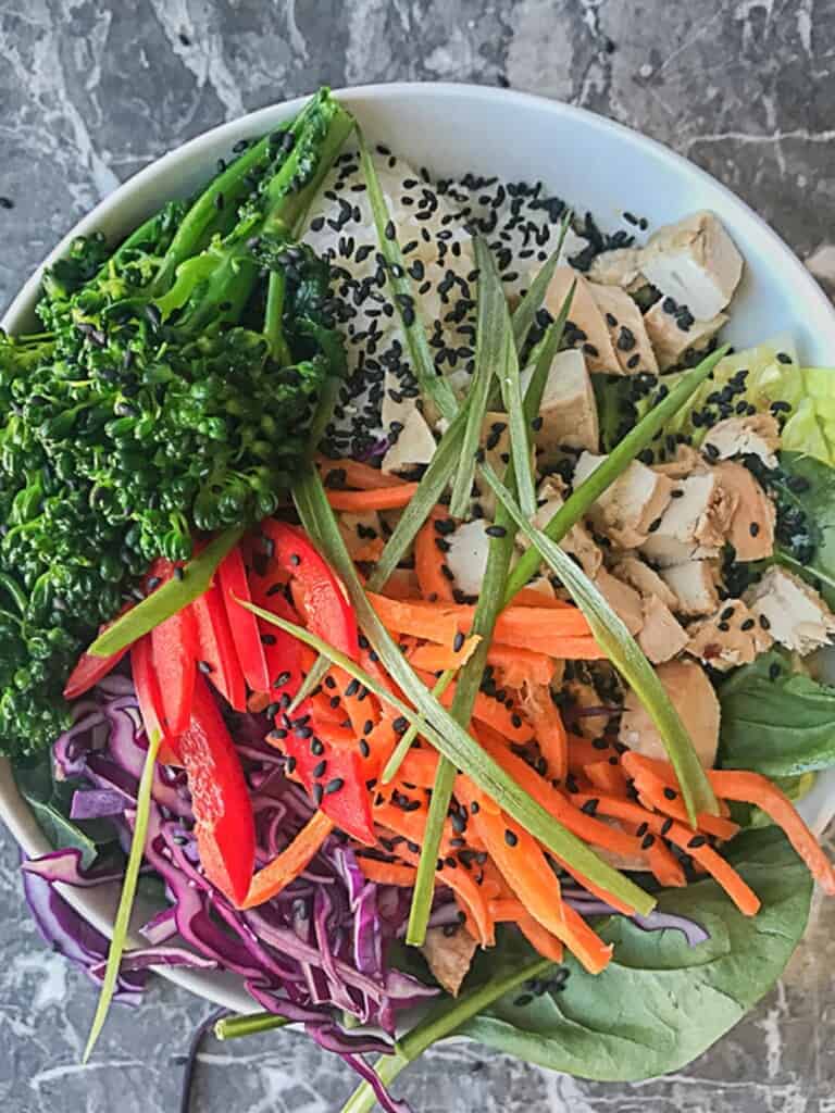 healthy teriyaki chicken and rice bowl with lots of veggies, topped with back sesame seeds and sesame ginger dresing