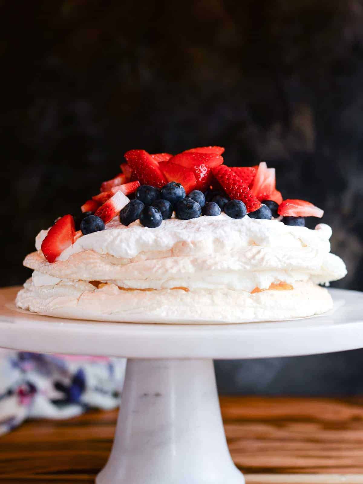 pavlova cake with lemon curd and fresh whipped cream presented on a marble cake stand